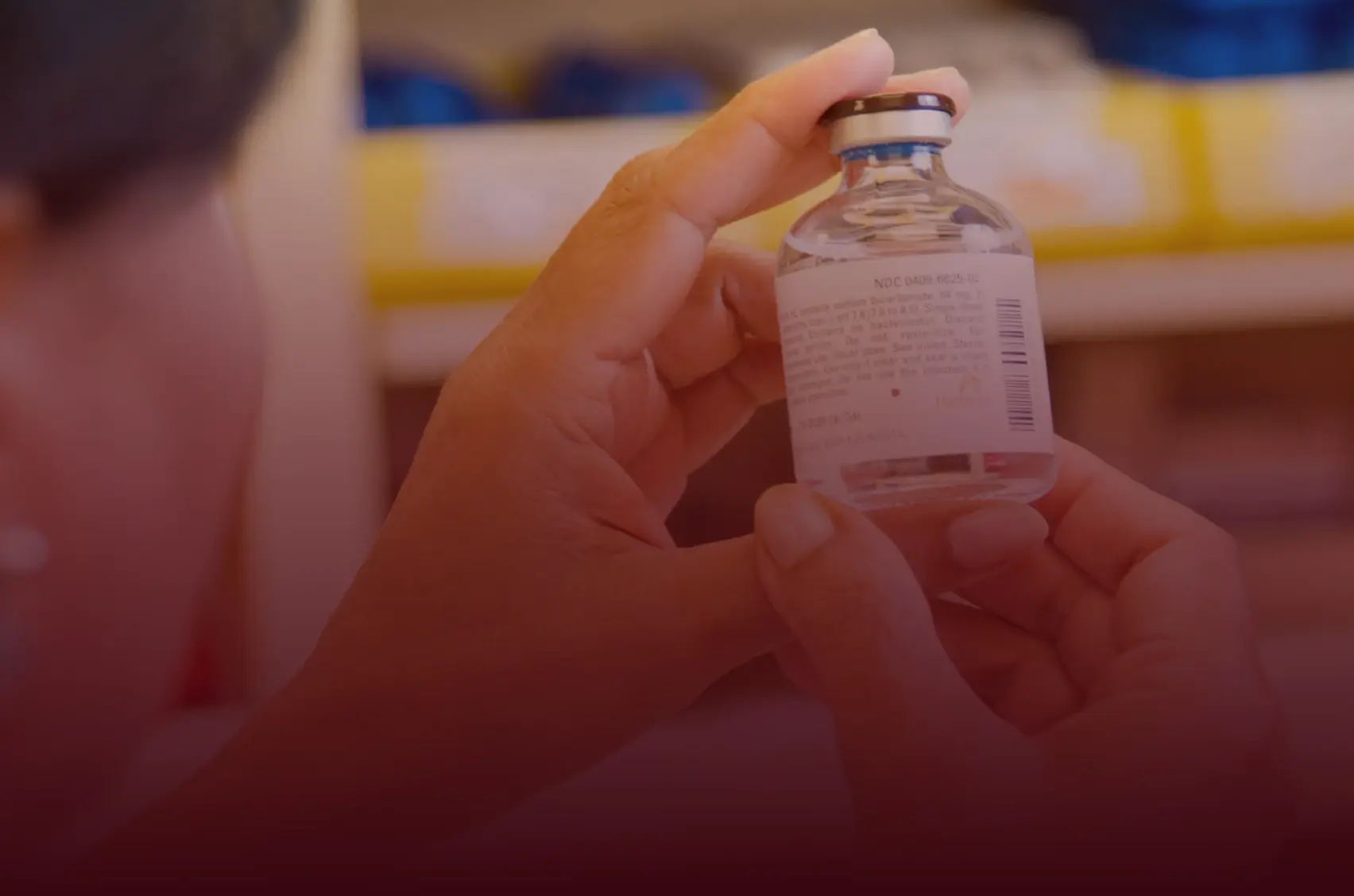 Photograph of a pharmacist handling a sealed medication vial in a compounding pharmacy