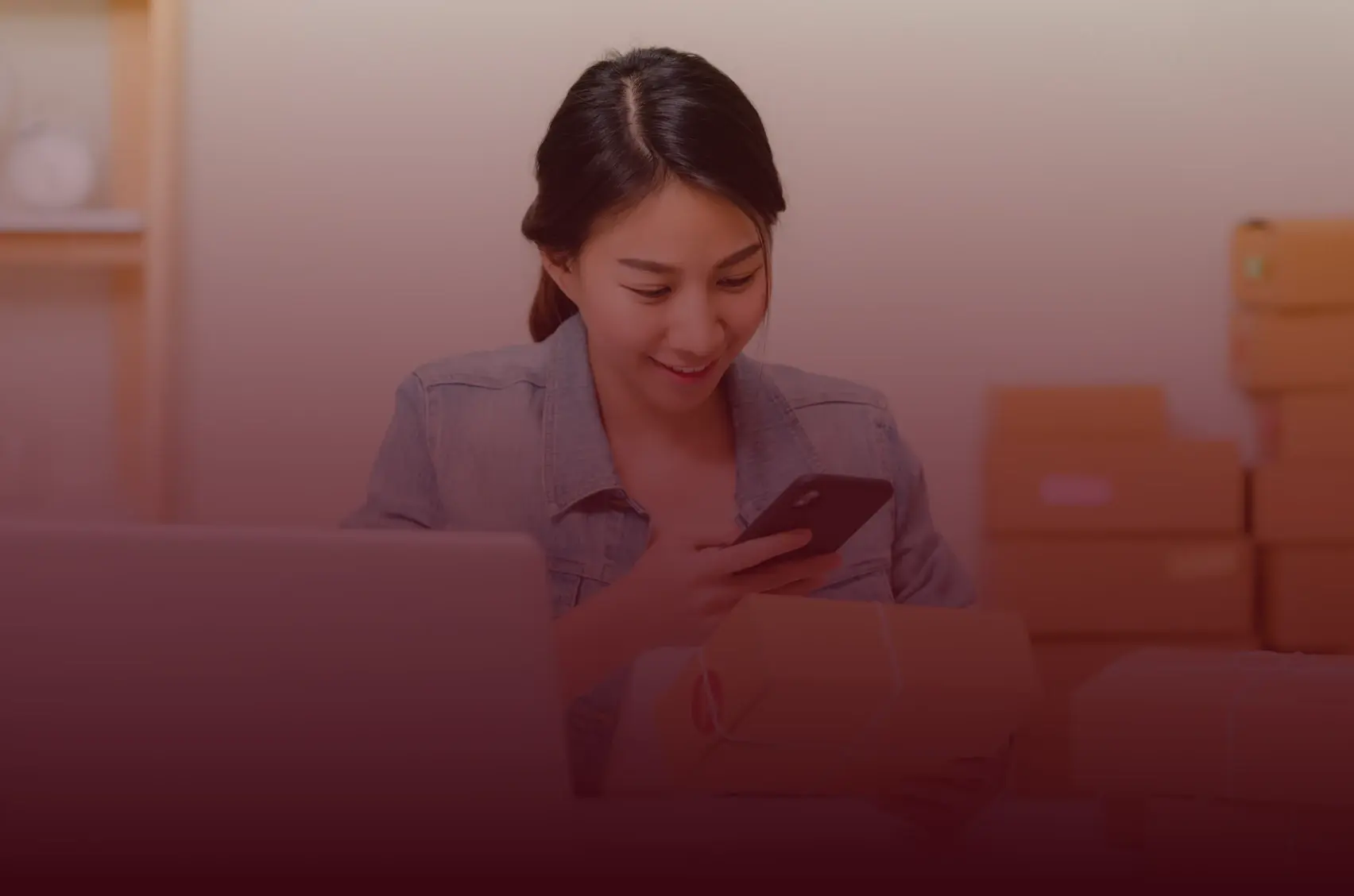 Photograph of a woman at home checking her phone beside delivered parcels